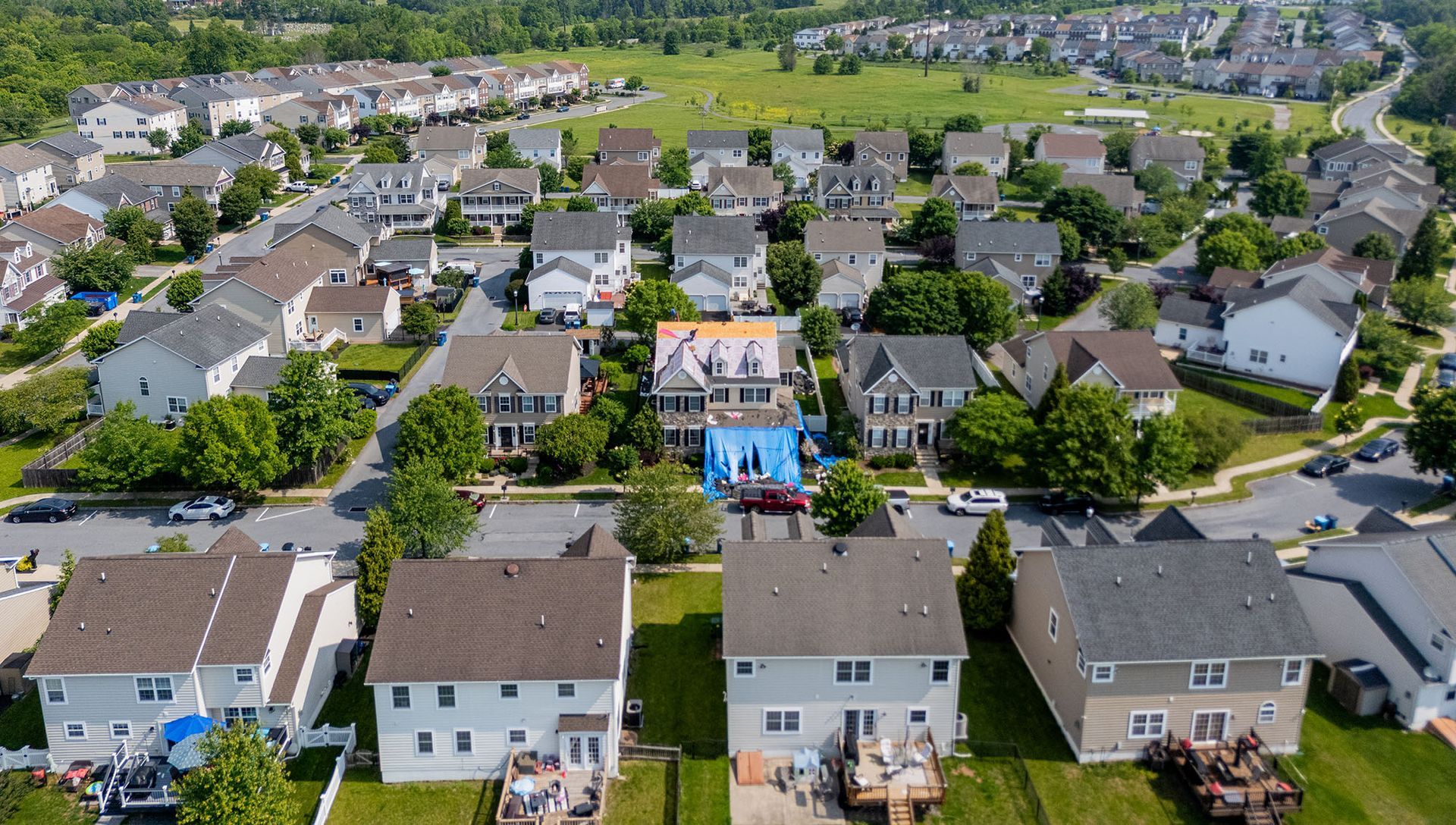 Aerial view of a suburban neighborhood with houses, green lawns, and a field in the background.