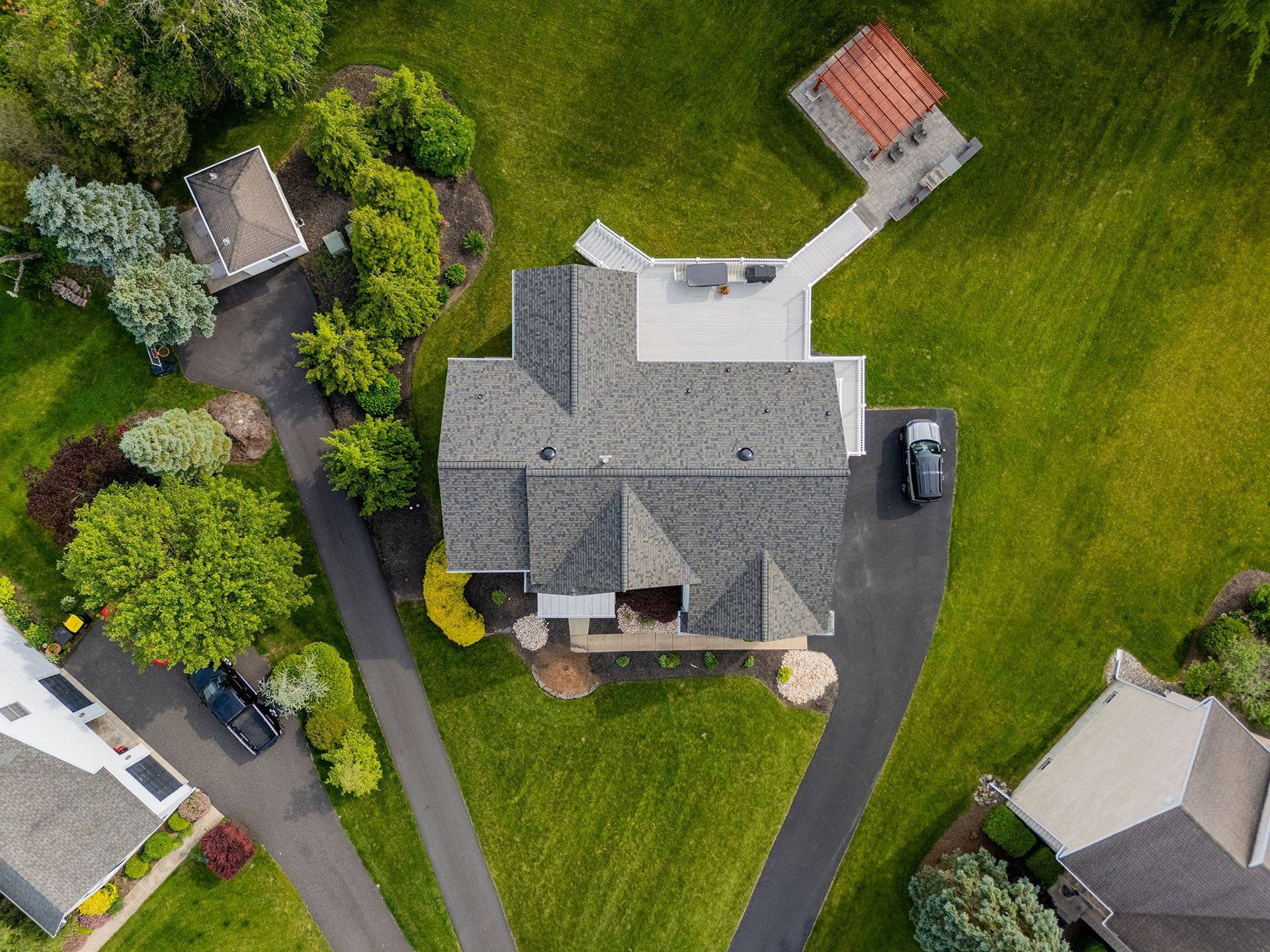 Overhead view of a house with a gray roof, black driveway, and surrounding green lawn.