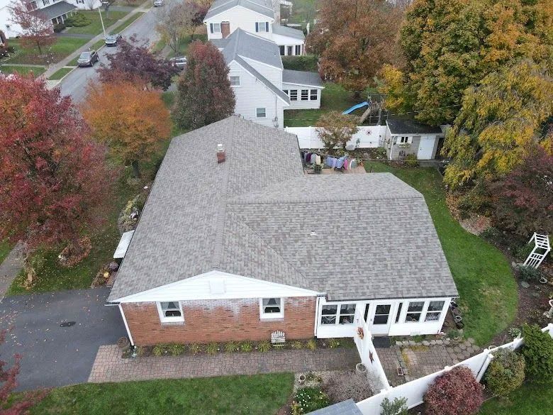 Aerial view of a suburban house with a gray roof, surrounded by trees with colorful autumn foliage.