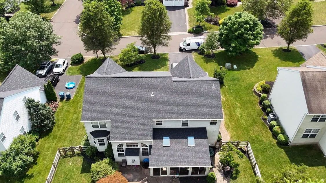 Aerial view of a gray-roofed house with a large lawn in a suburban neighborhood.
