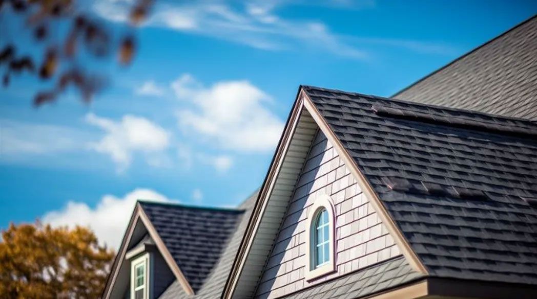 Dark gray shingled roof with light brown trim against a bright blue sky with fluffy white clouds.