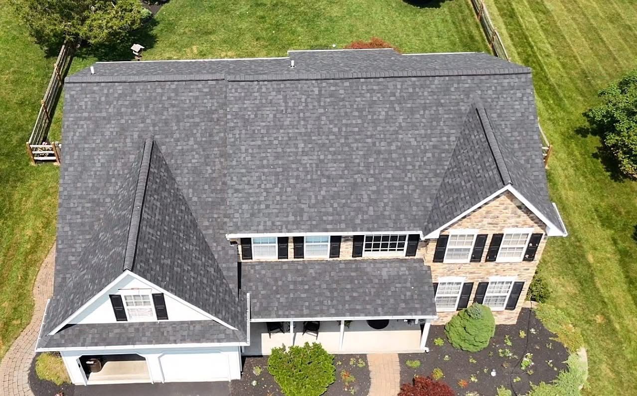 Aerial view of a house with a gray shingle roof, surrounded by green grass.