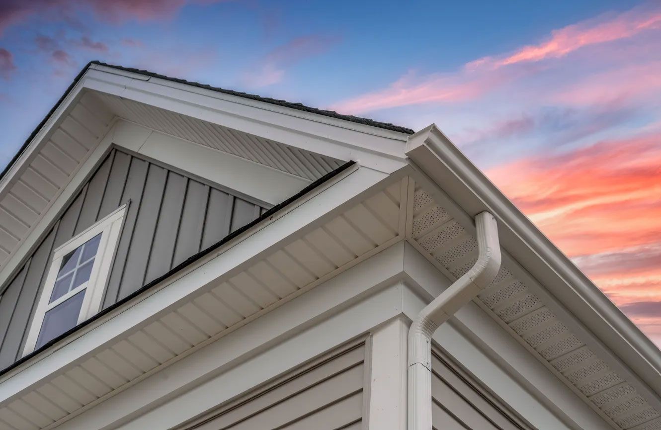 White house exterior with grey siding, white trim, and a gutter, against a sunset sky.