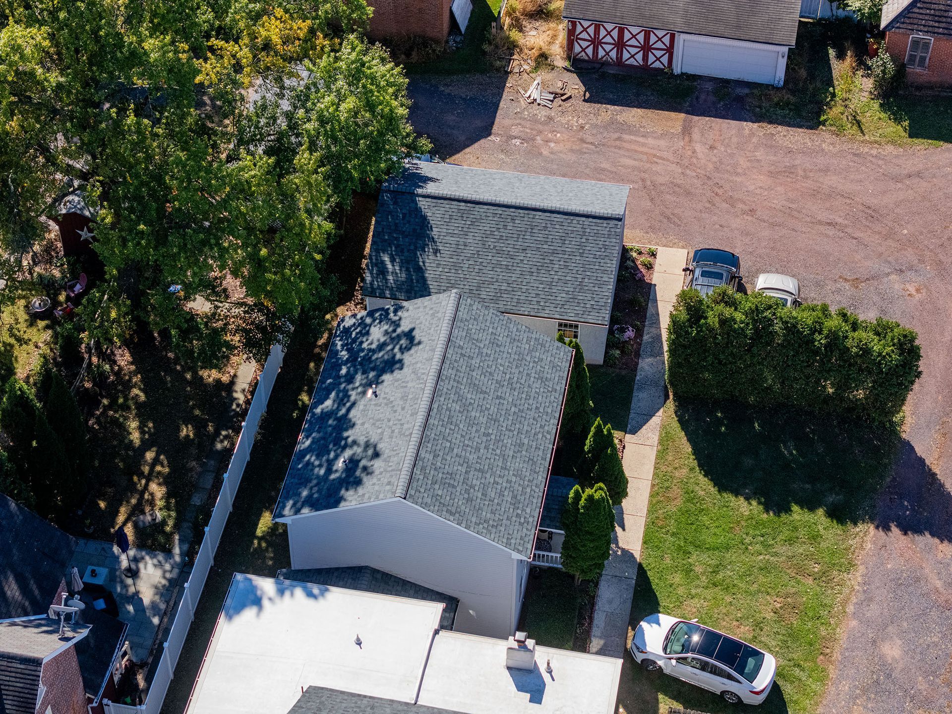 Aerial view of a house with a dark gray roof, next to a garage, with a small yard, trees, and cars.