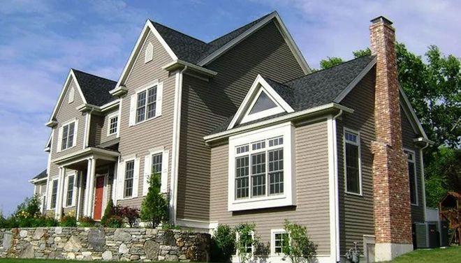 Two-story house with brown siding, black roof, brick chimney, and stone foundation.
