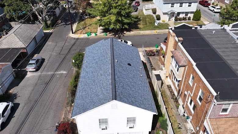 Aerial view of a house with a dark blue roof, street and surrounding buildings.