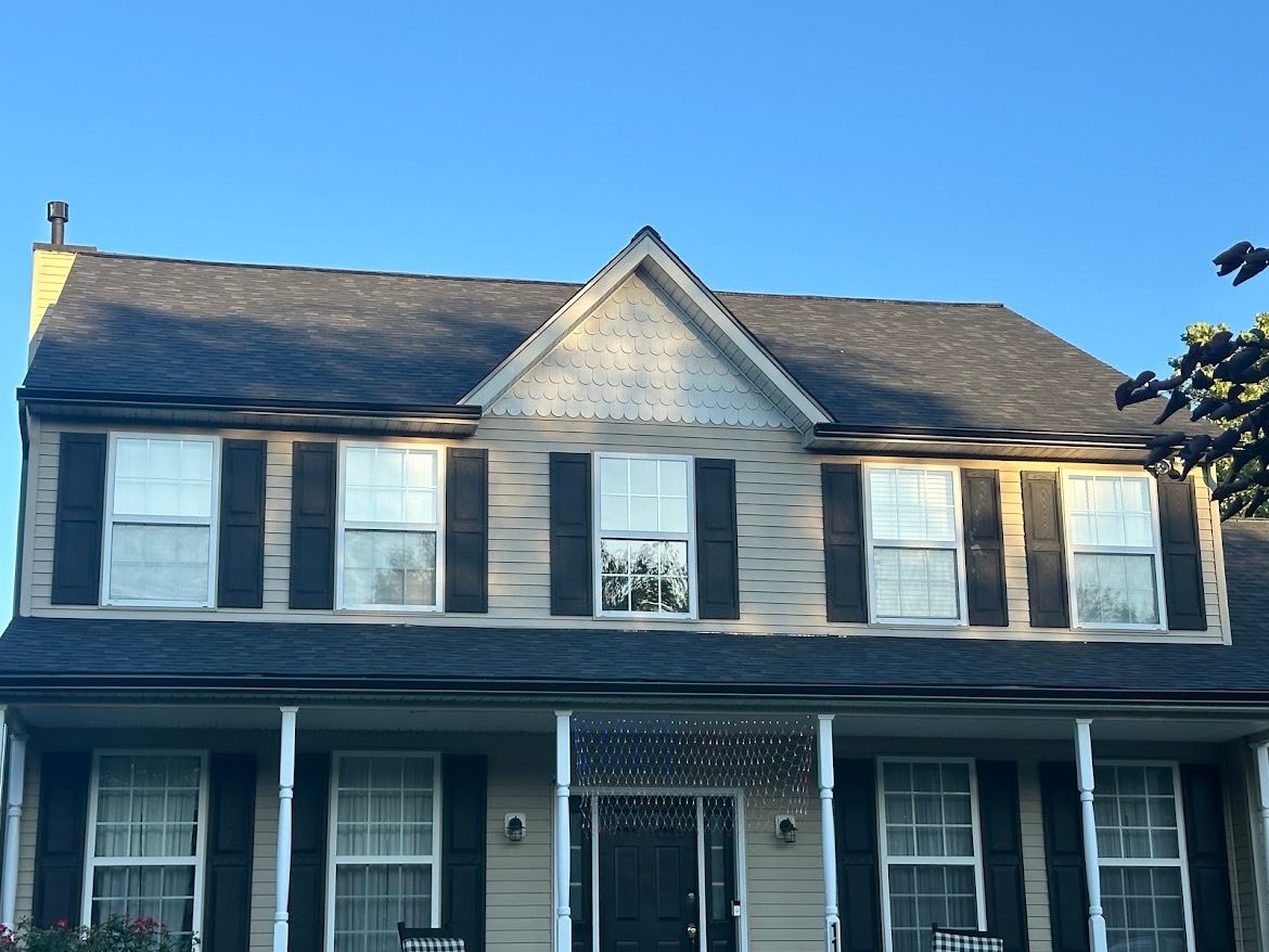 Two-story beige house with black shutters and a porch, set against a clear blue sky.