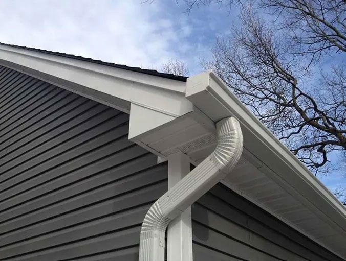 White gutters and downspout on a house with gray siding under a cloudy sky.