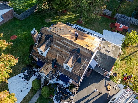 Aerial view of house roof being repaired; workers on the roof, debris on ground, blue tarp, sunny day.