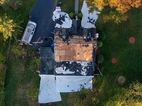 Overhead view of a house roof partially covered with tarp during a roofing project; a truck and equipment are nearby.