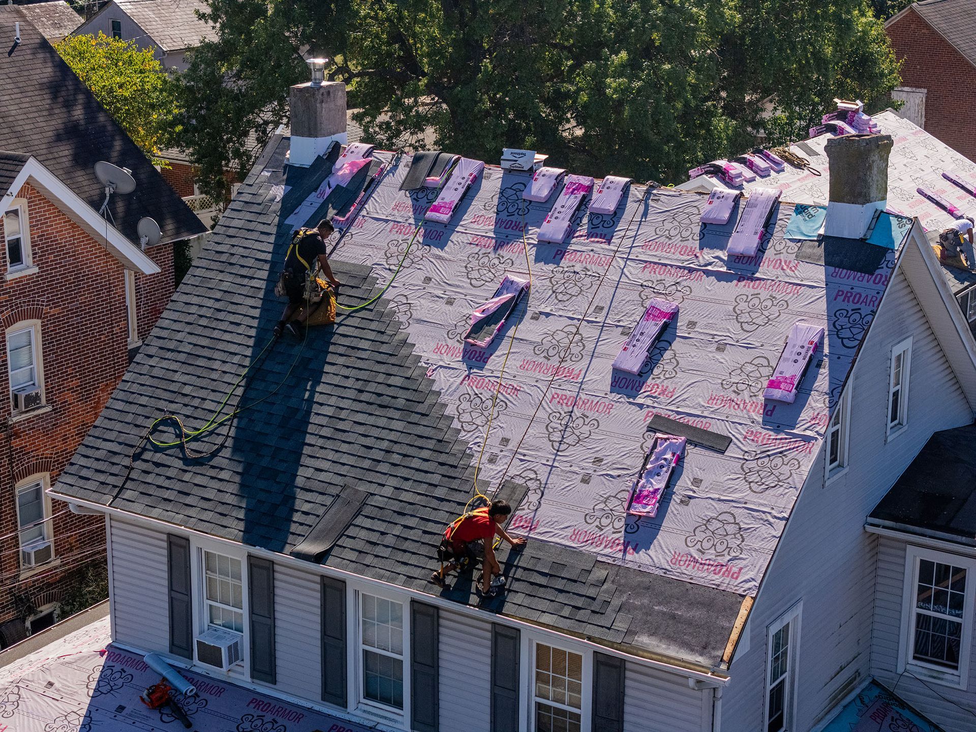 Two roofers installing new shingles on a house roof with pink insulation.