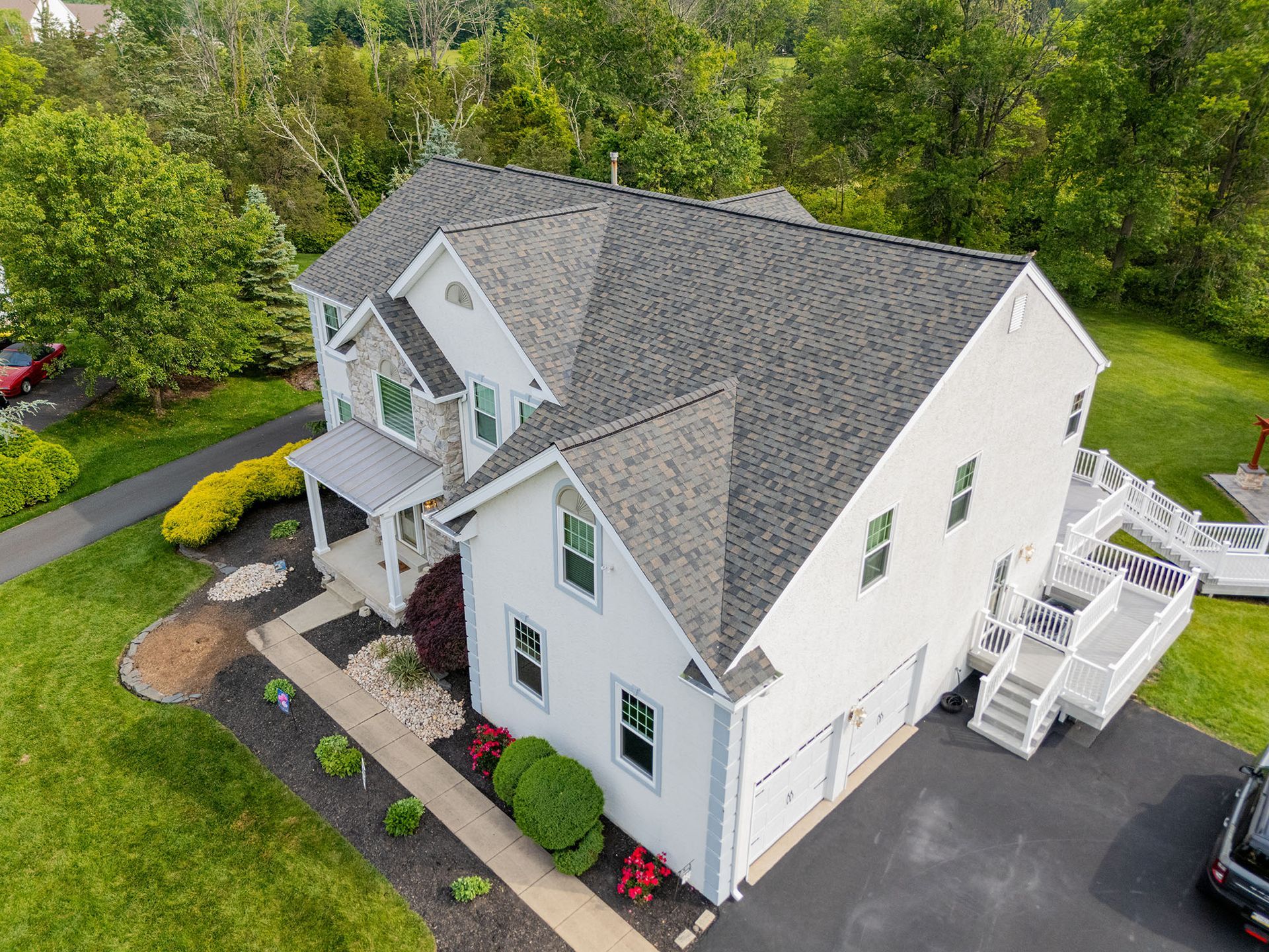 White two-story house with gray roof, front porch, attached garage, and surrounding landscaping.