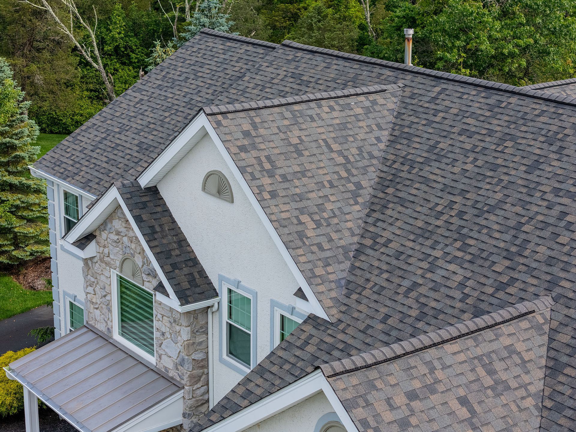 Gray asphalt shingle roof on a house with stone and white siding.