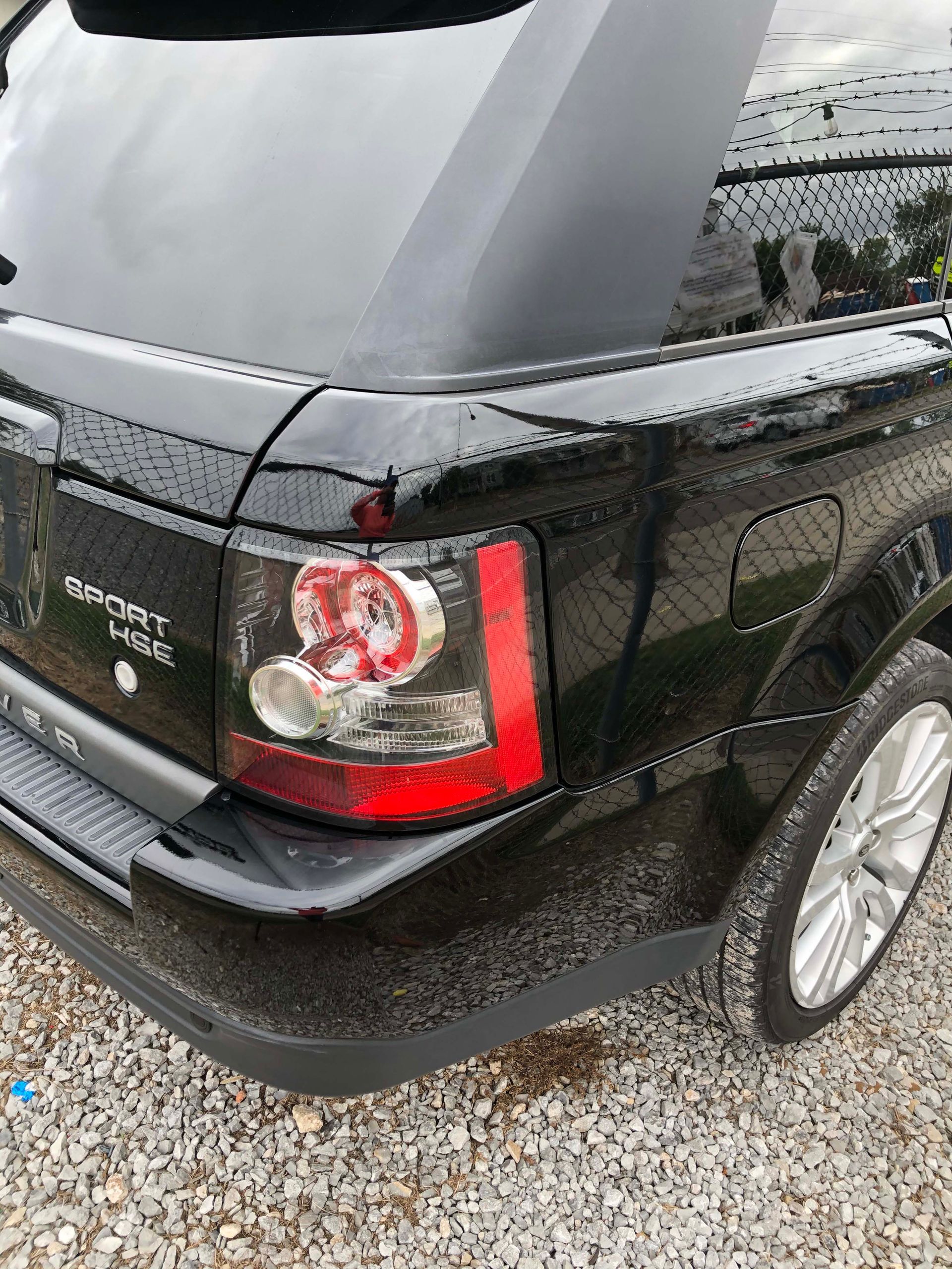 A black range rover sport is parked on gravel.