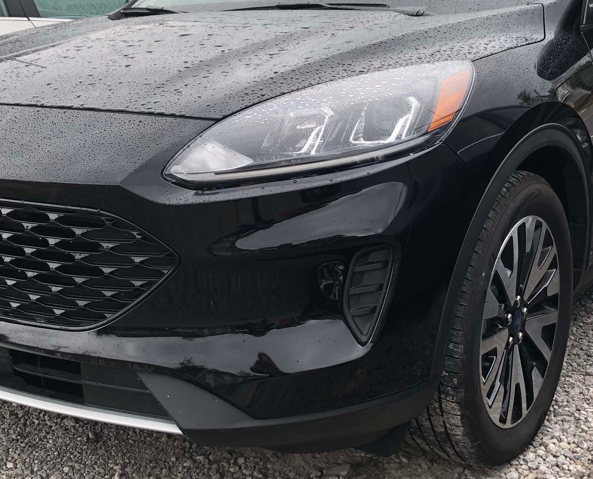 A black ford escape is parked on gravel in the rain.