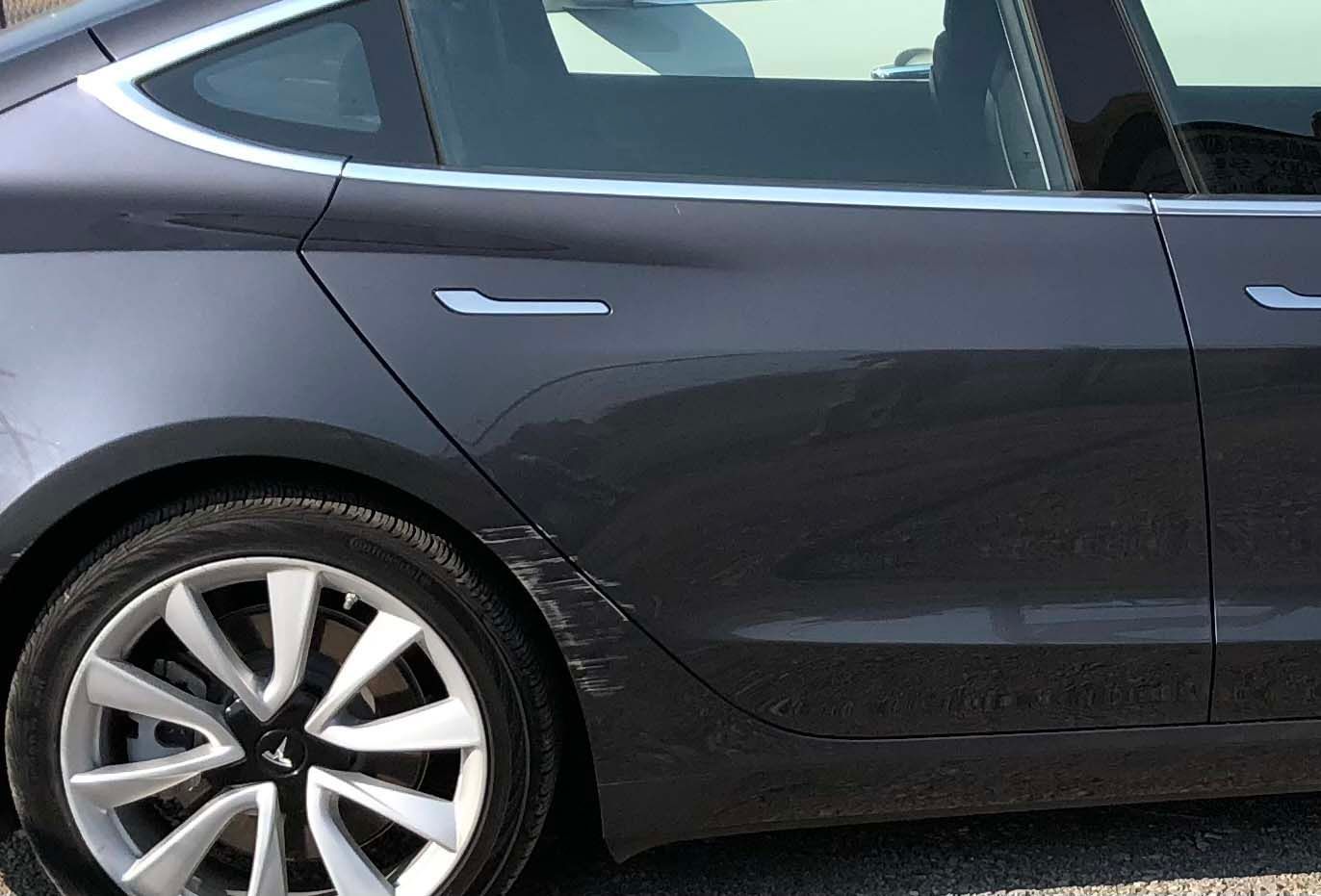 A tesla model 3 is parked on the side of the road