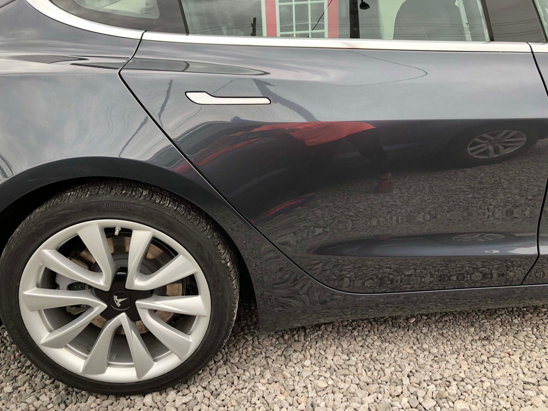 A close up of a tesla model 3 parked on gravel.