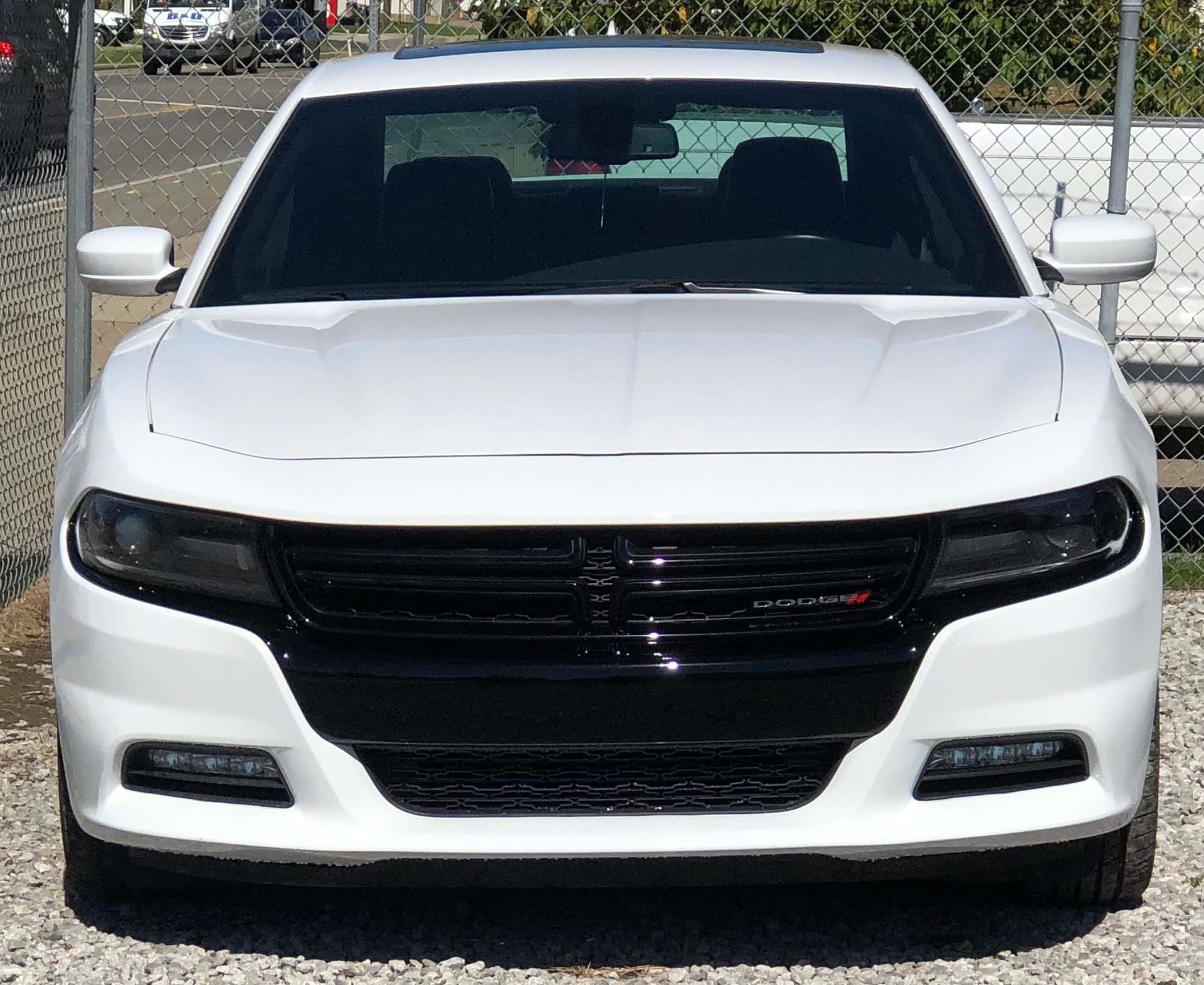 A white dodge charger is parked in front of a chain link fence