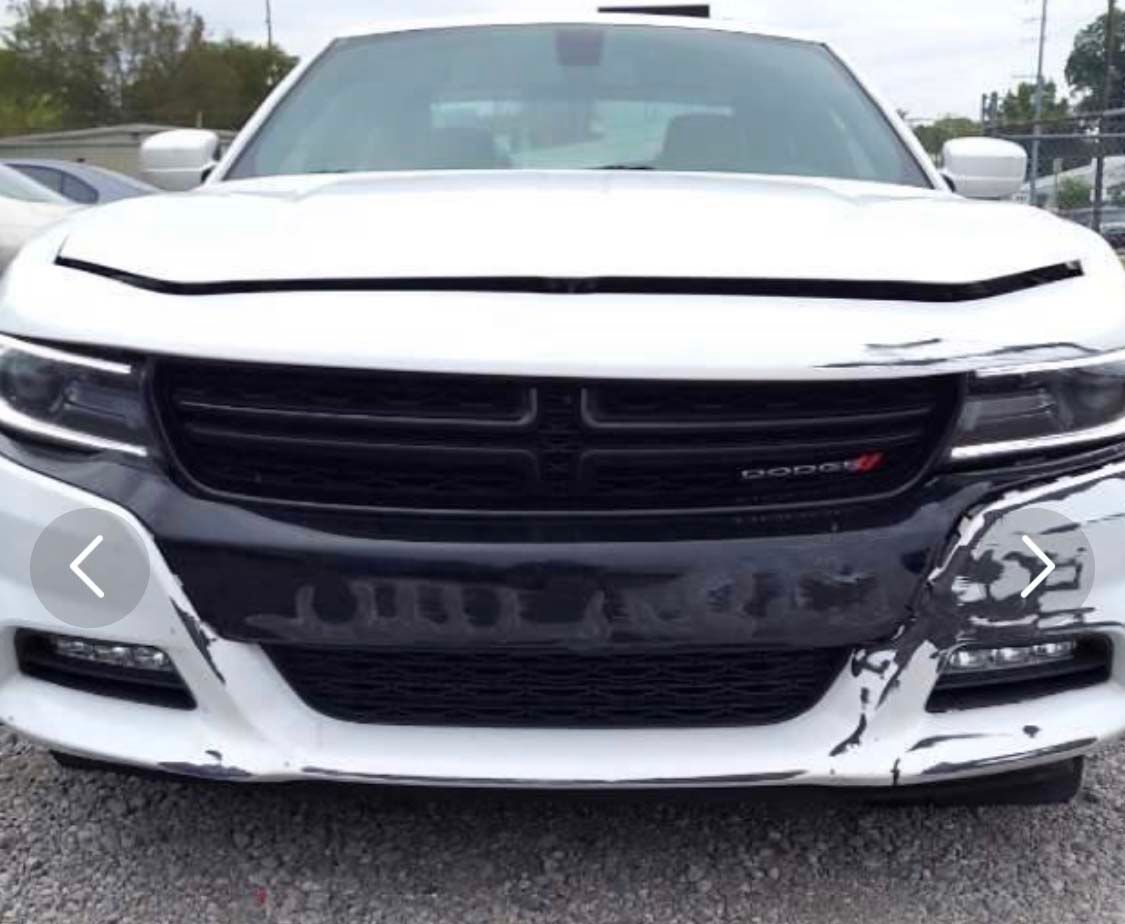 A white dodge charger with a damaged front bumper is parked in a parking lot.