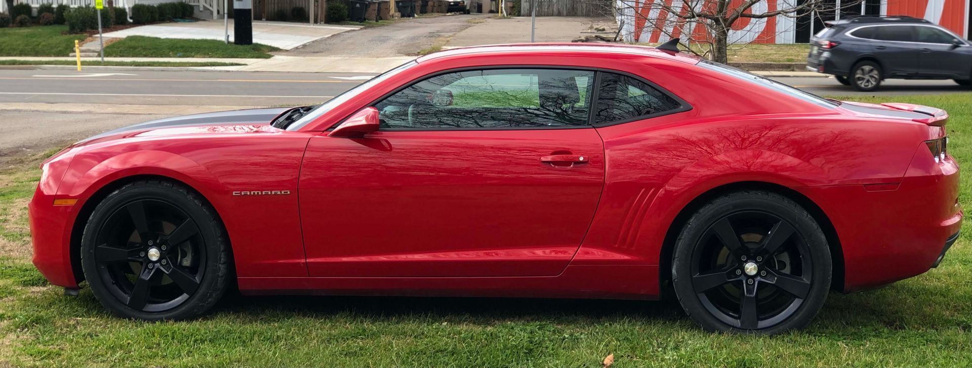 A red car is parked in the grass on the side of the road.