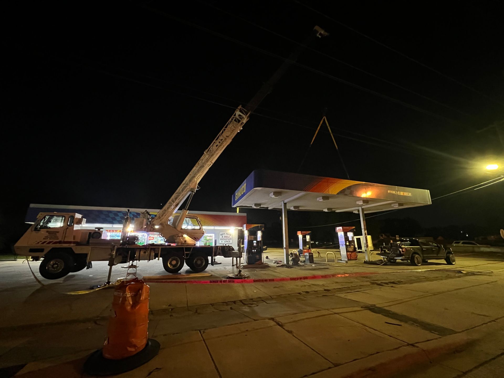 Crane at a gas station at night, possibly removing or installing canopy structure.