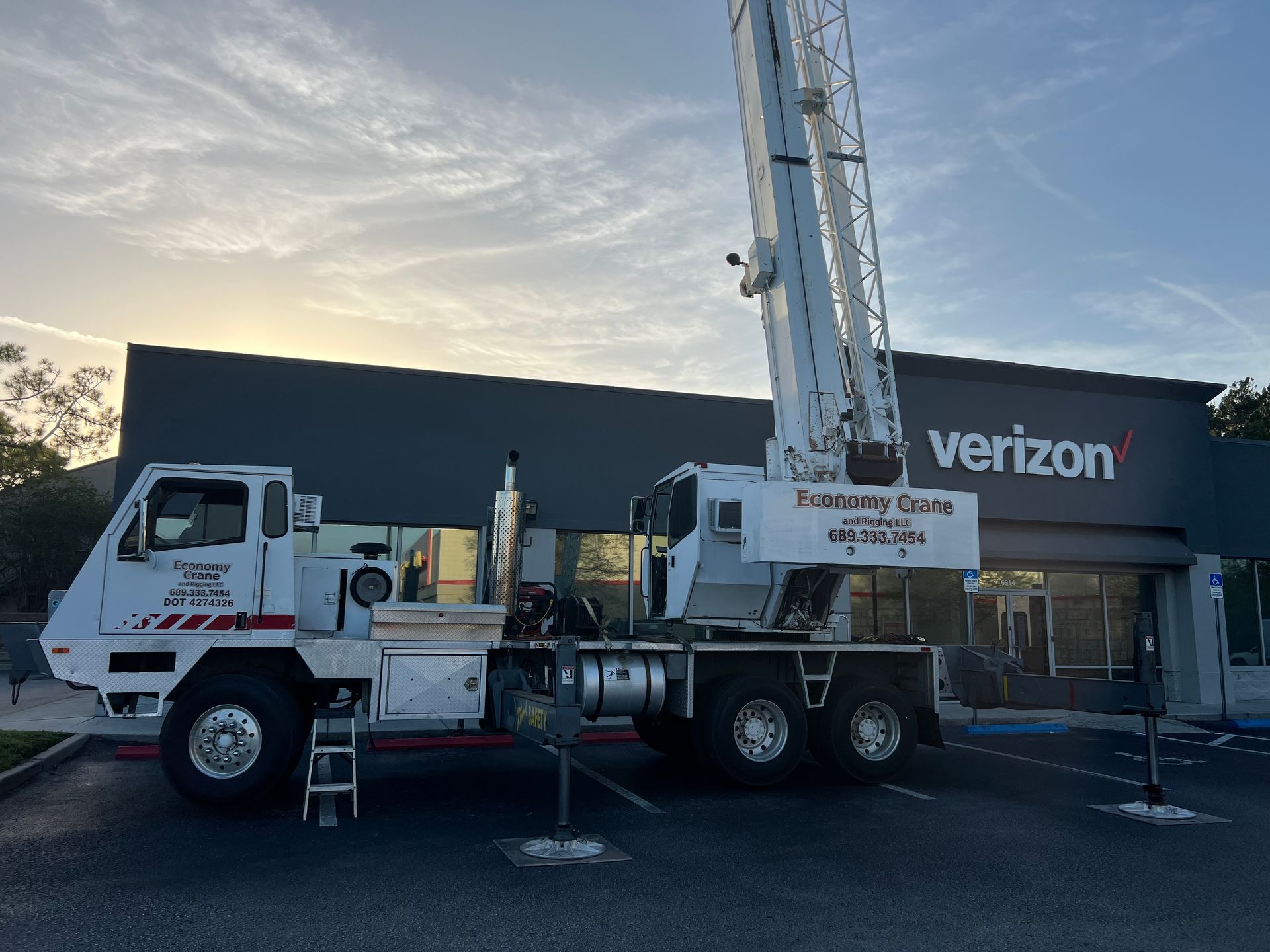White crane truck parked outside a Verizon store with a cloudy sky in the background.