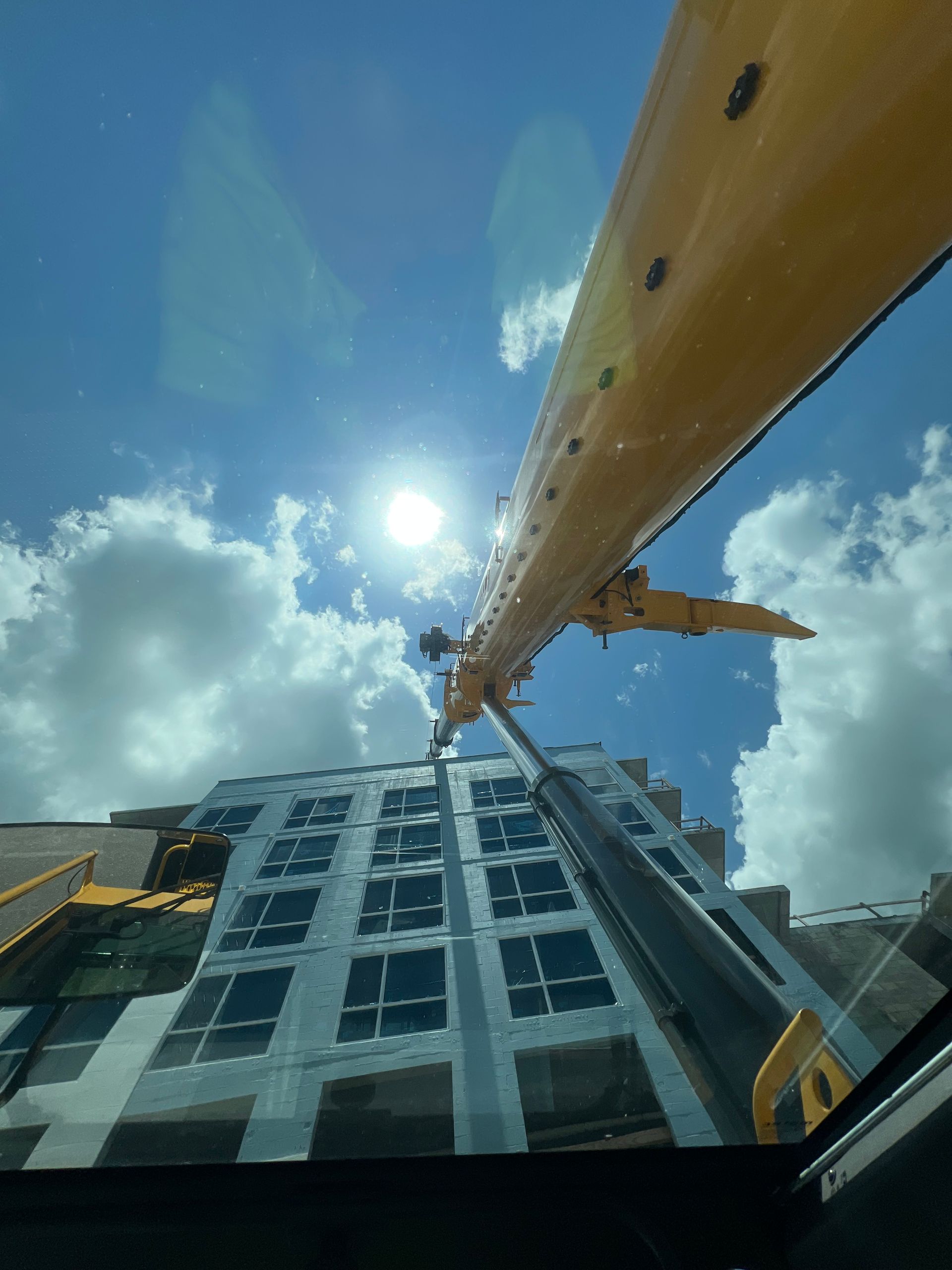 A crane reaching towards a high-rise building on a sunny, partly cloudy day.