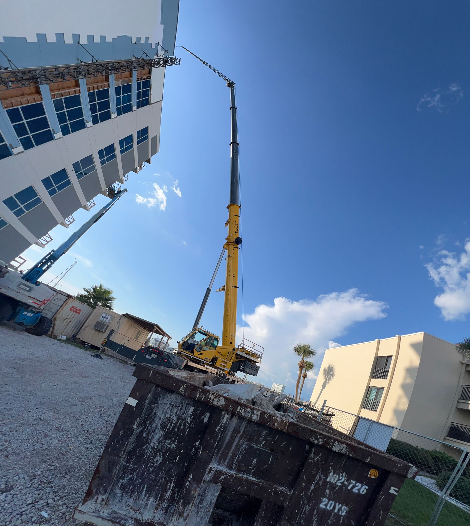 Crane lifting debris from construction site next to tall buildings under blue sky.