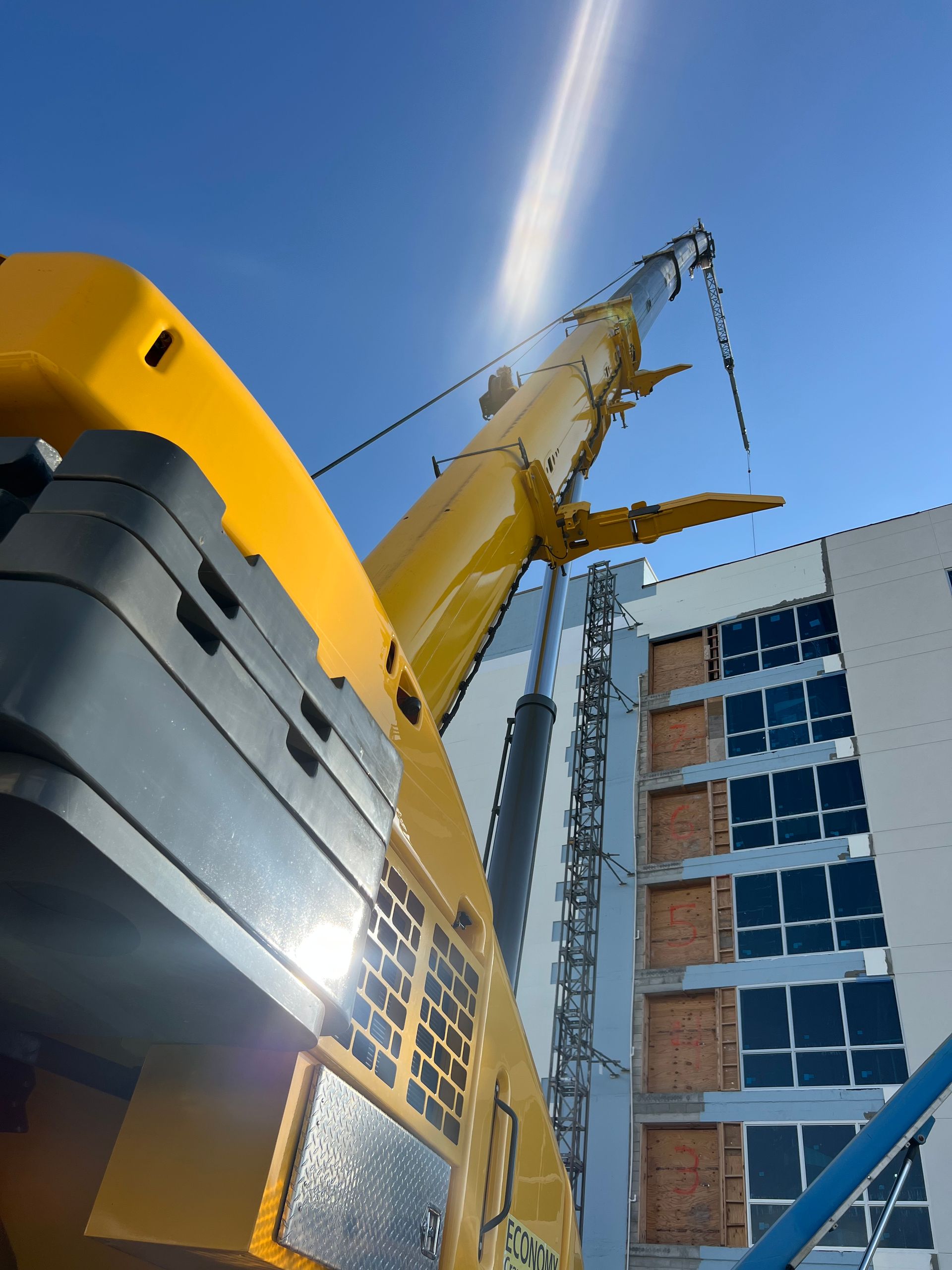 Yellow crane extending towards a building with the sun in the background.