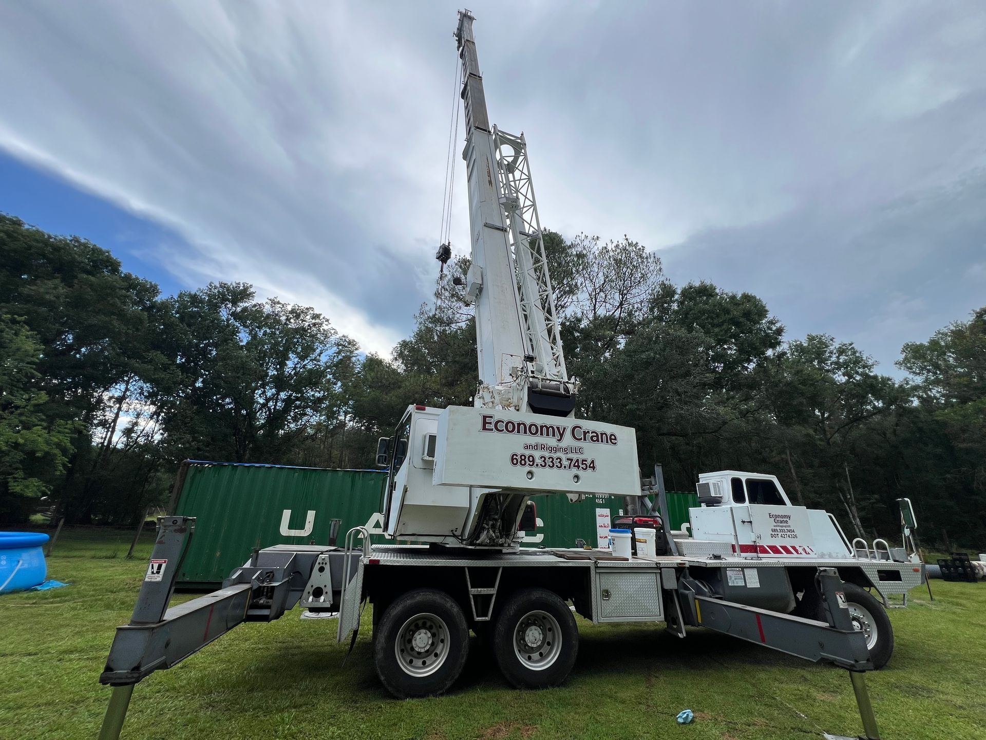 A white crane truck with its arm extended in a grassy outdoor setting.