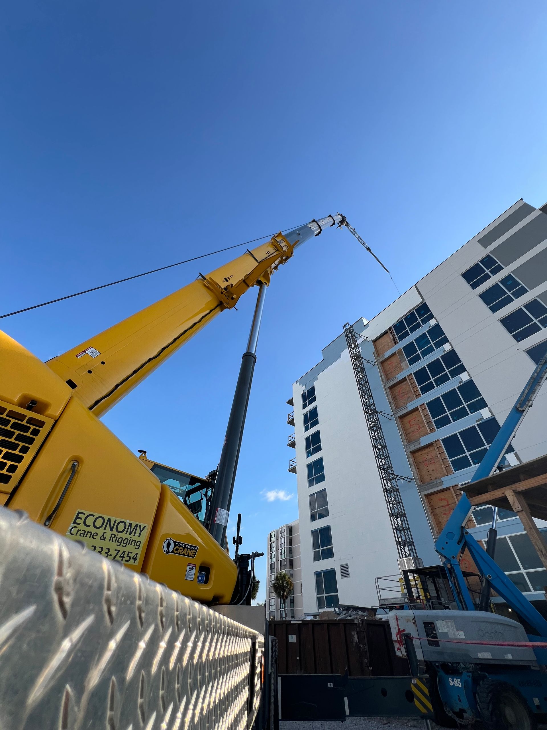 Yellow crane extending towards a high-rise building under construction against a blue sky.