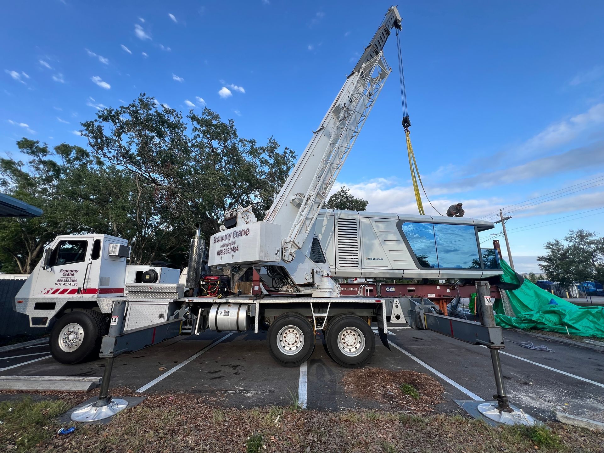 A white crane truck lifts a large object on a sunny day.