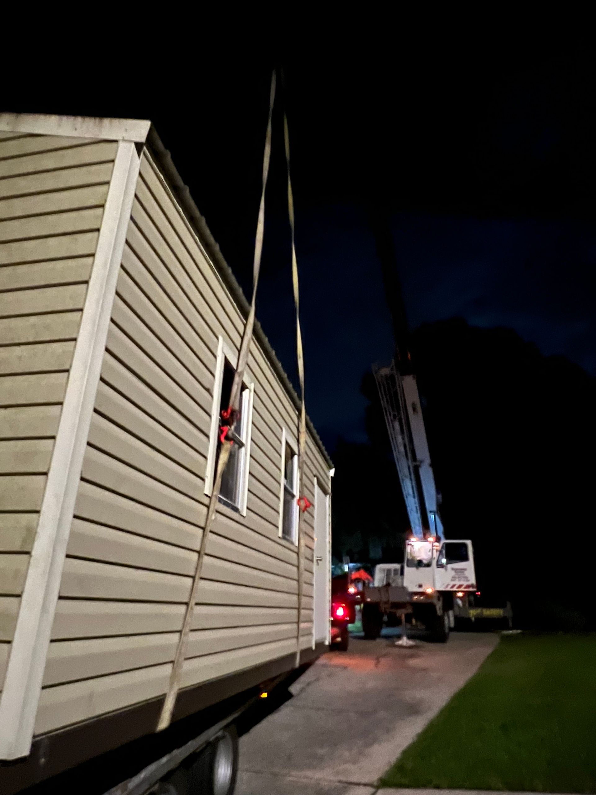 A modular building being lifted by a crane at night; a truck is attached.