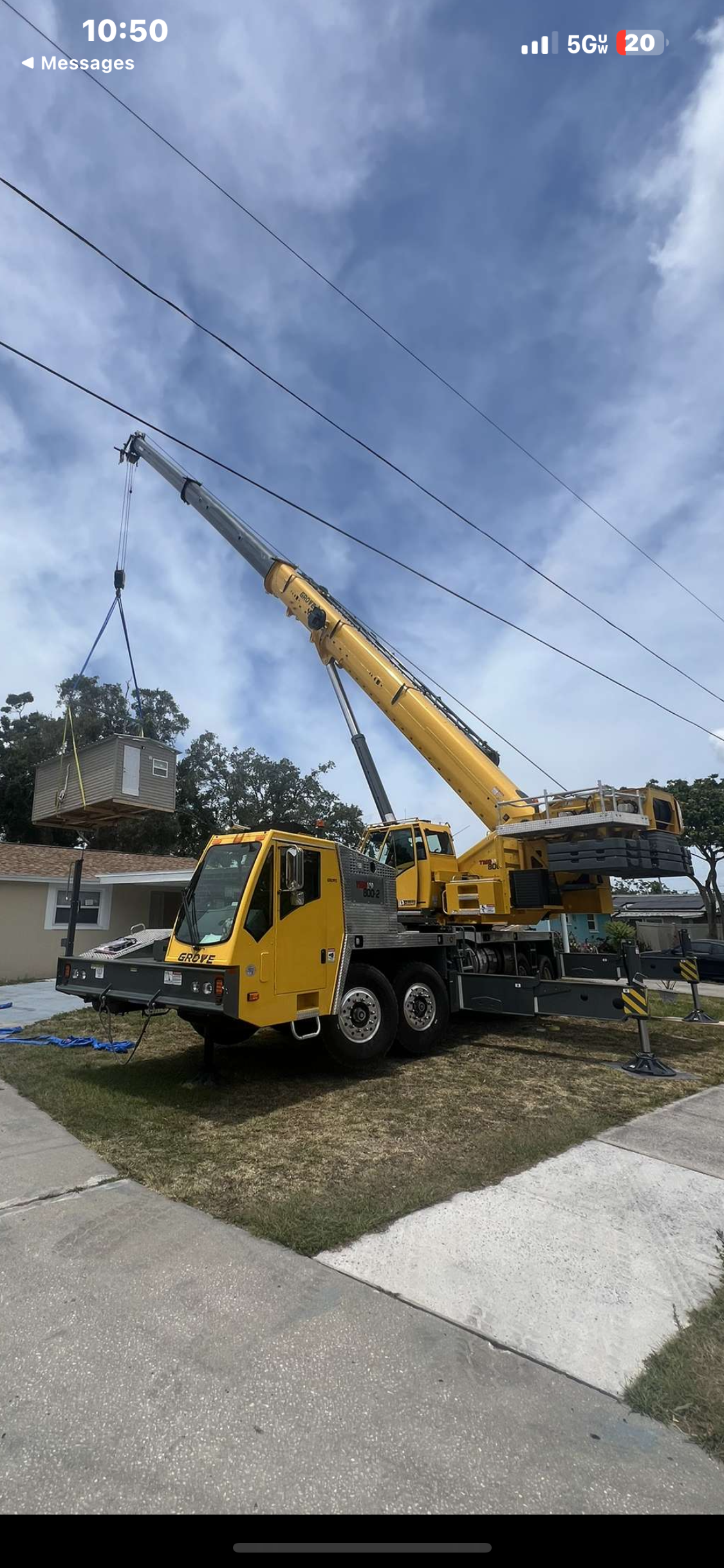 A yellow crane lifting a large object, possibly a container, against a cloudy sky.