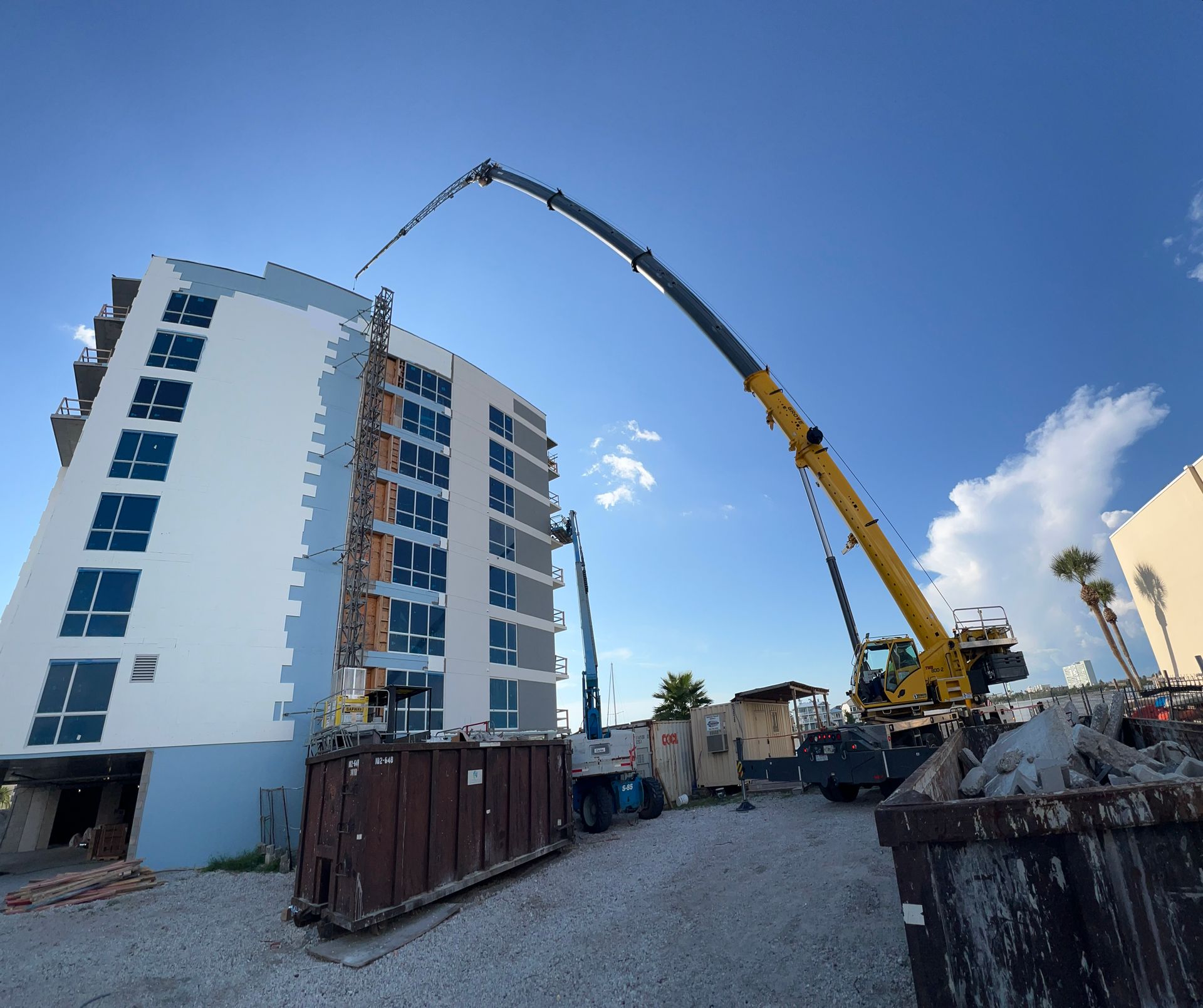 Construction site with a crane extending over a multi-story building under a bright blue sky.