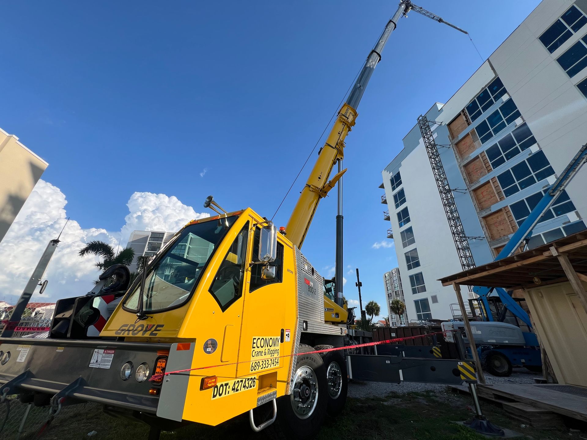 Yellow crane next to a building under construction on a sunny day with a blue sky.
