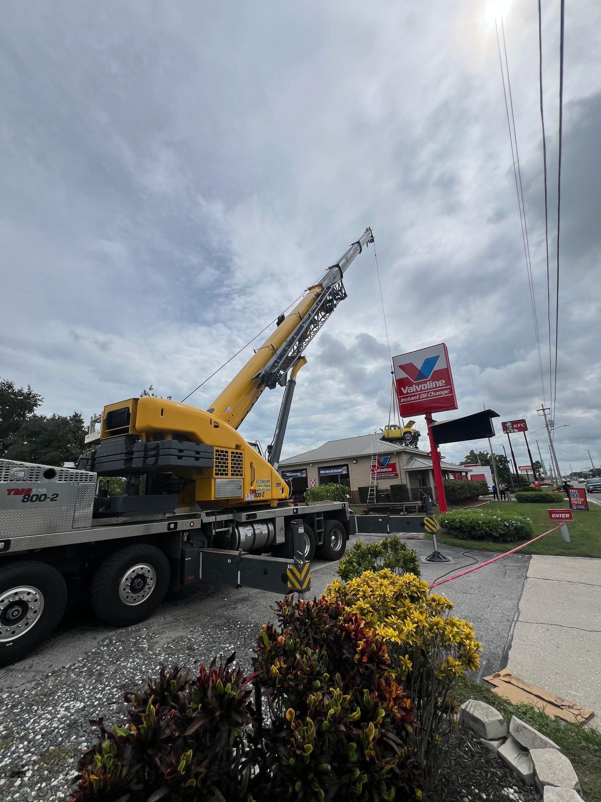 Yellow crane at a McDonald's, likely for signage work, with power lines overhead on a cloudy day.