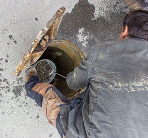 Man lifting bucket of debris from sewer