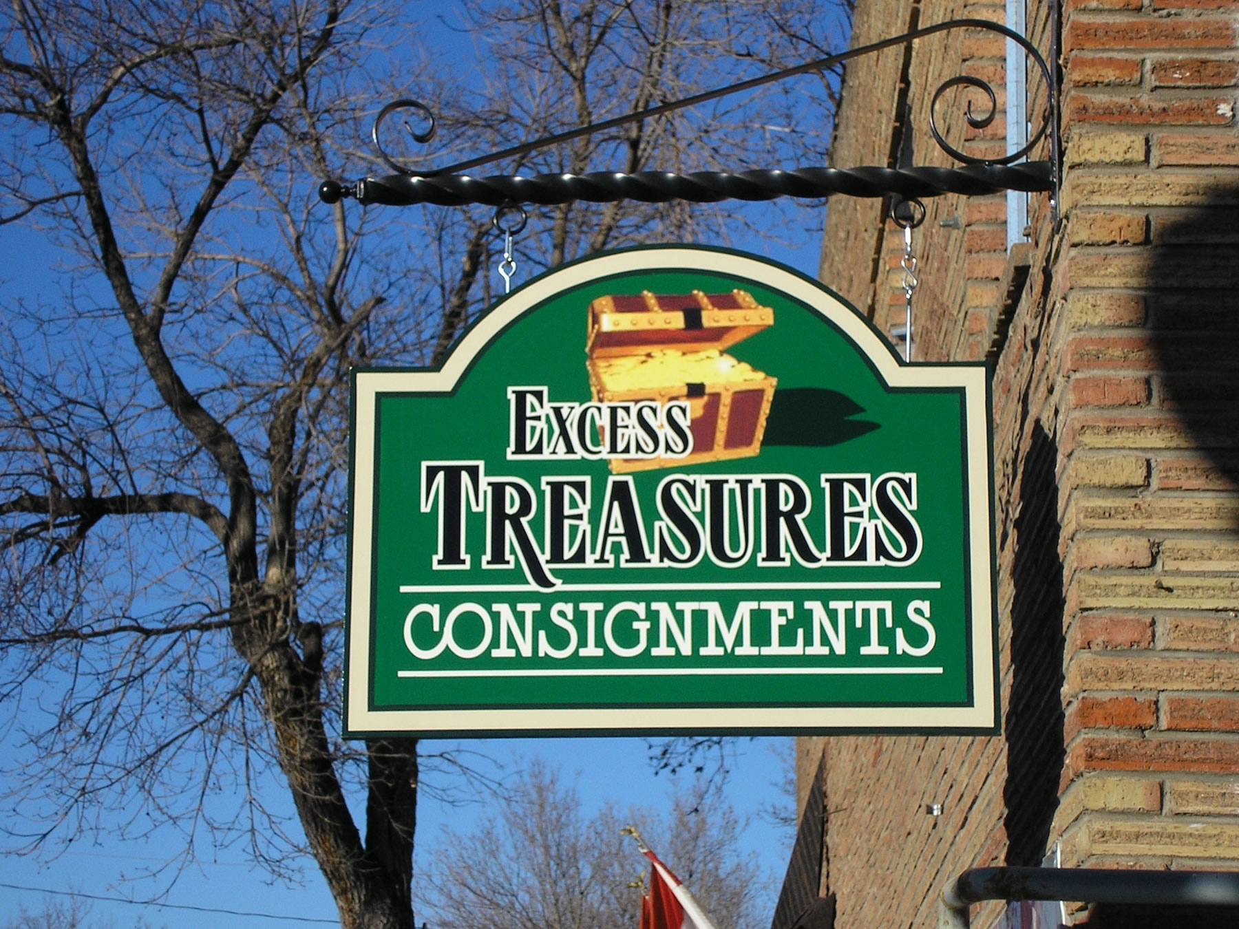 A sign for excess treasures consignments hangs from a brick building