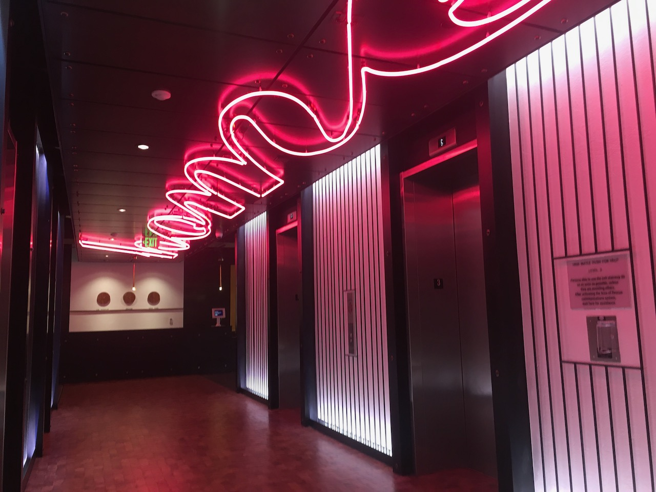 A hallway with elevators and a neon sign on the ceiling
