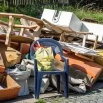 Pile of discarded furniture and waste, including a blue chair and a yellow bag.