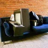 A vintage television and speaker sit on a dark blue couch against a brick wall.