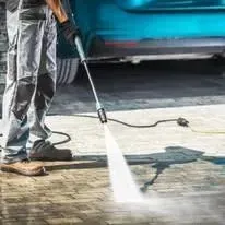 Person power washing a car's tire on a brick surface. Water sprays from a pressure washer.