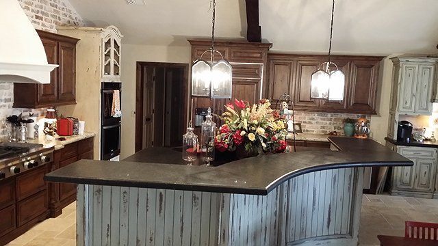 Rustic kitchen with dark countertops, wood cabinets, exposed brick, and a central island with a floral arrangement.