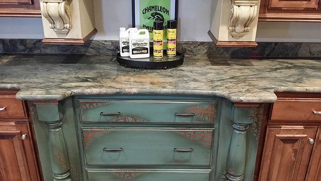 Kitchen counter with green and brown cabinets, holding cleaning products.