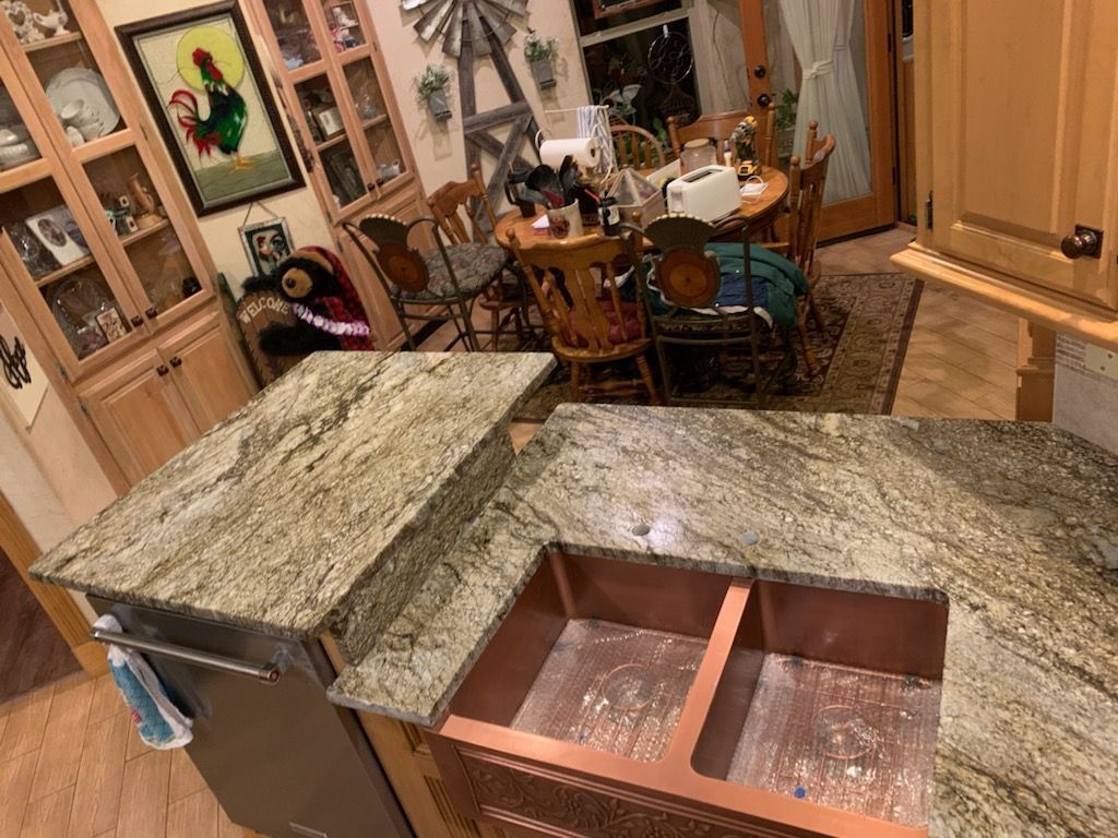 Kitchen island with a copper sink, granite countertops, and a dining area in the background.