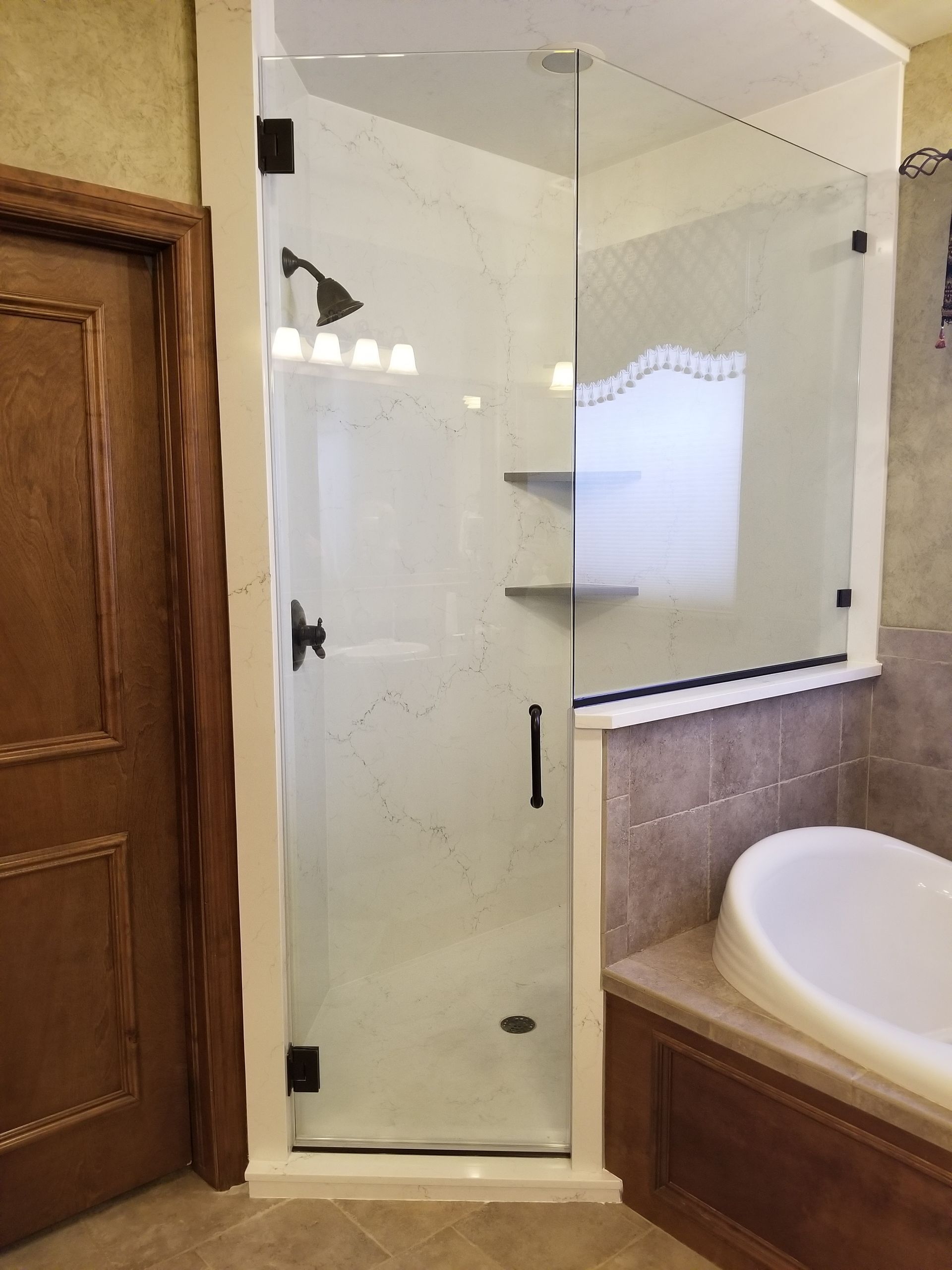 Glass shower enclosure with black fixtures and a white interior next to a bathtub.