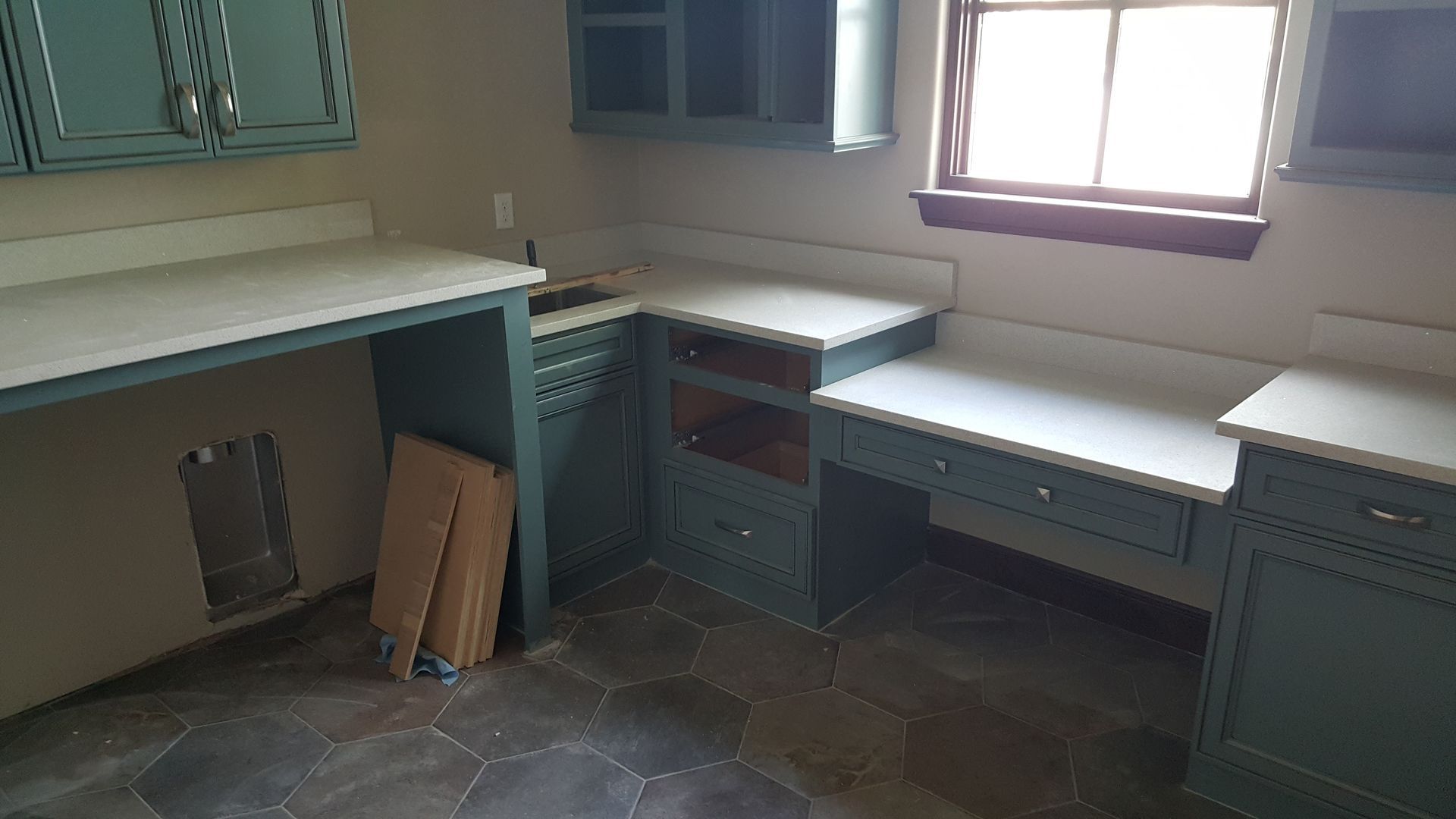 Blue cabinetry and white countertops in an unfinished room with stone floor and a window.