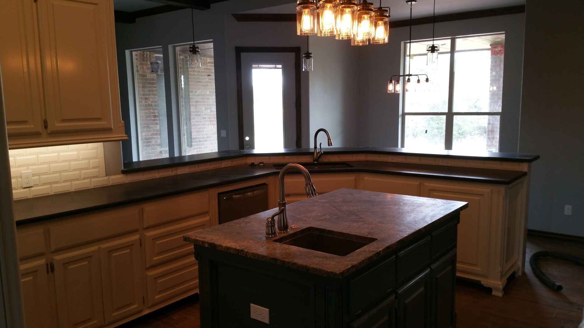 Kitchen with island, cream cabinets, dark countertops, and light fixture over the island.