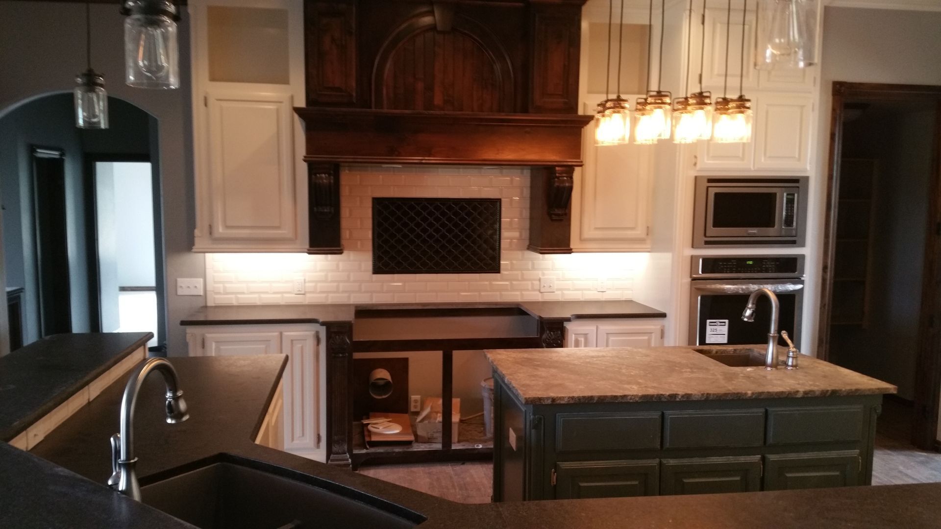 Kitchen with white cabinets, dark countertops, wooden range hood, and green island.